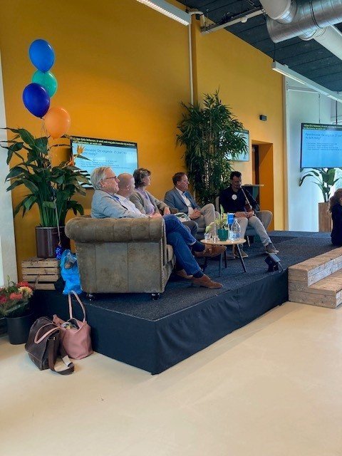 Ihab and four other participants sit on sofas on the stage during the panel discussion, with a small table in front of them.