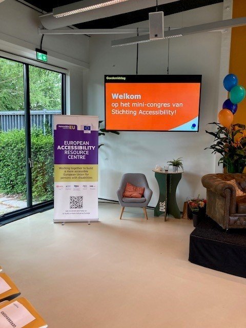 Conference room with a Stichting Accessibility welcome screen, an AccessibleEU banner, chairs and colourful balloons.