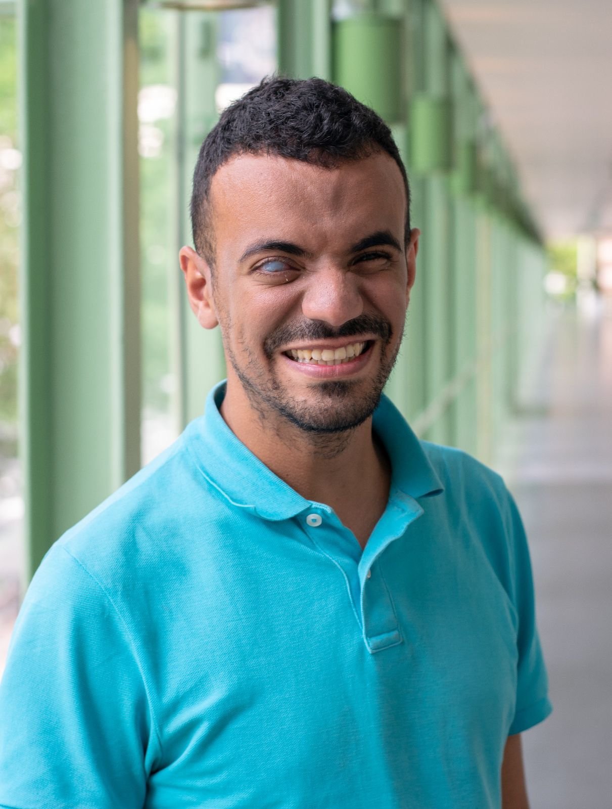 Ihab Laachir smiling in a turquoise polo shirt, with windows in the background.