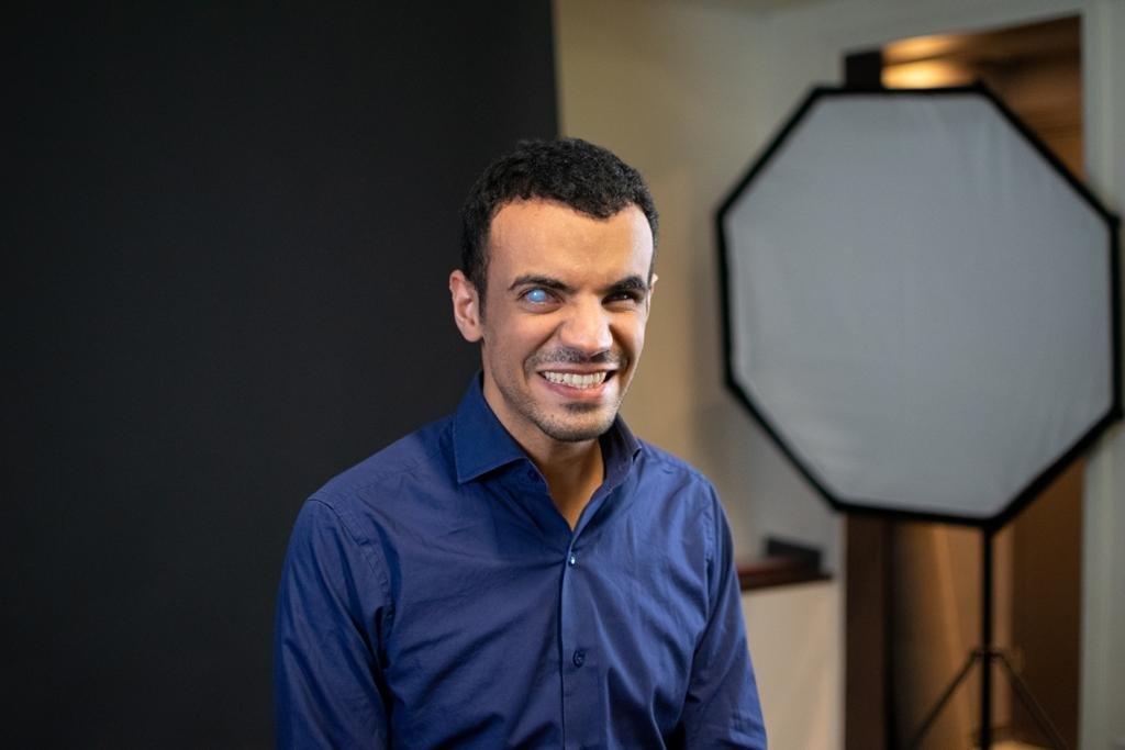 Ihab Laachir sonríe con una camisa azul oscuro. Detrás de él hay una gran luz de fotografía.